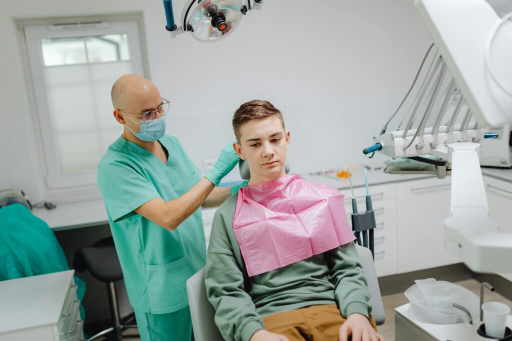 A teenager in a dental chair receiving care from a masked dentist.